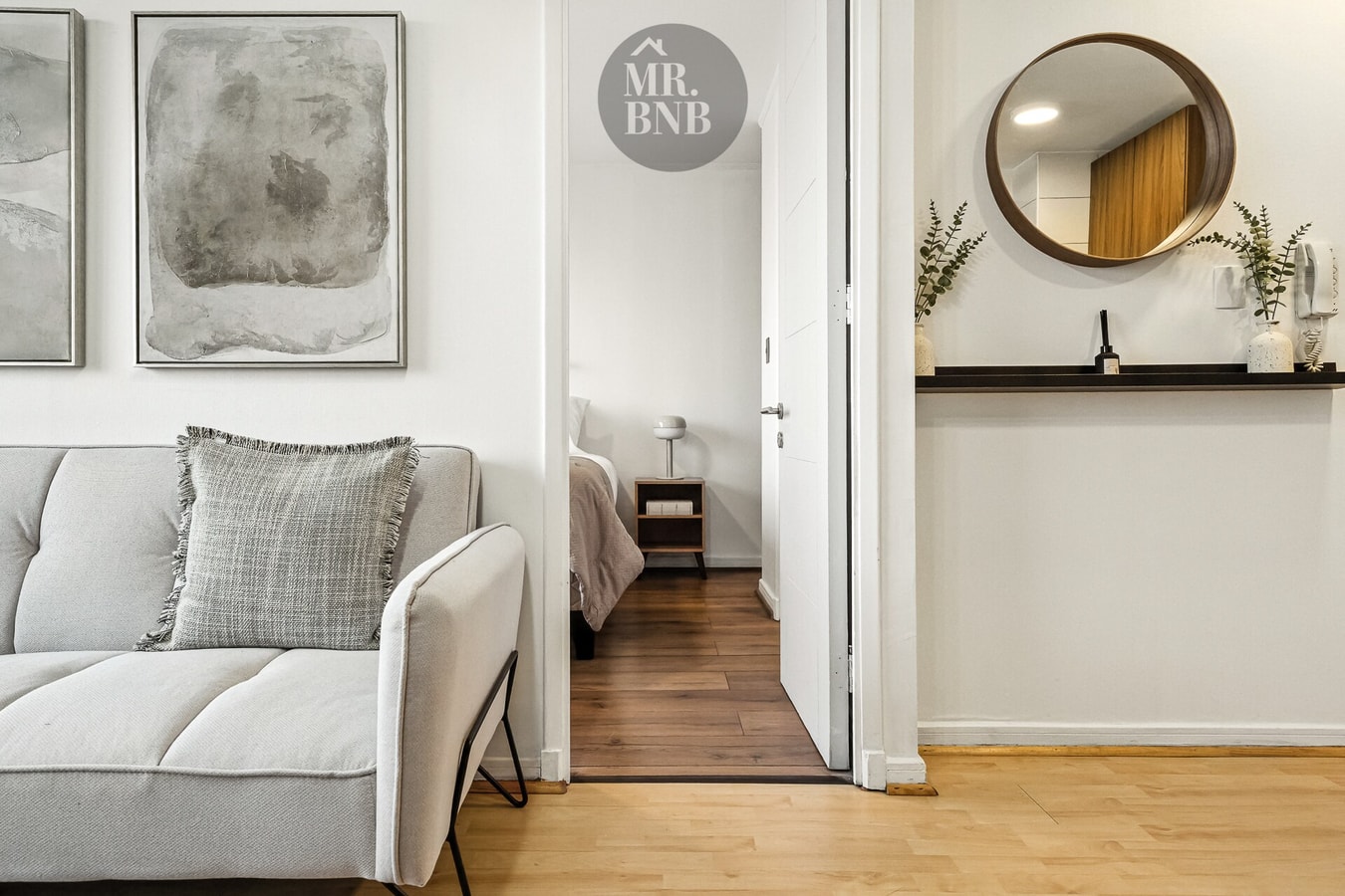 Living con sofá y acceso a dormitorio y pasillo, con cuadro y espejo redondo en la entrada