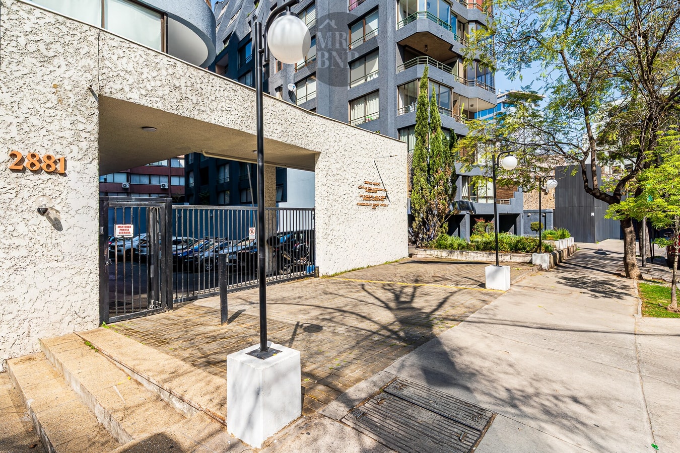 Acceso y fachada del edificio con jardineras y vereda arbolada