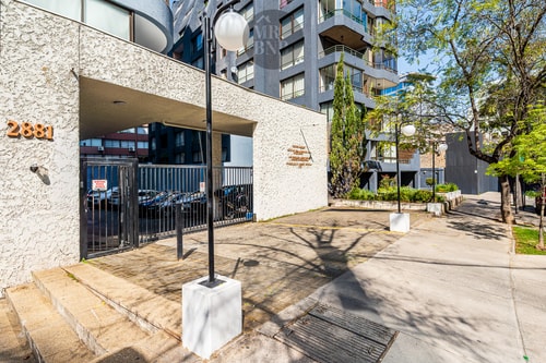 Acceso y fachada del edificio con jardineras y vereda arbolada