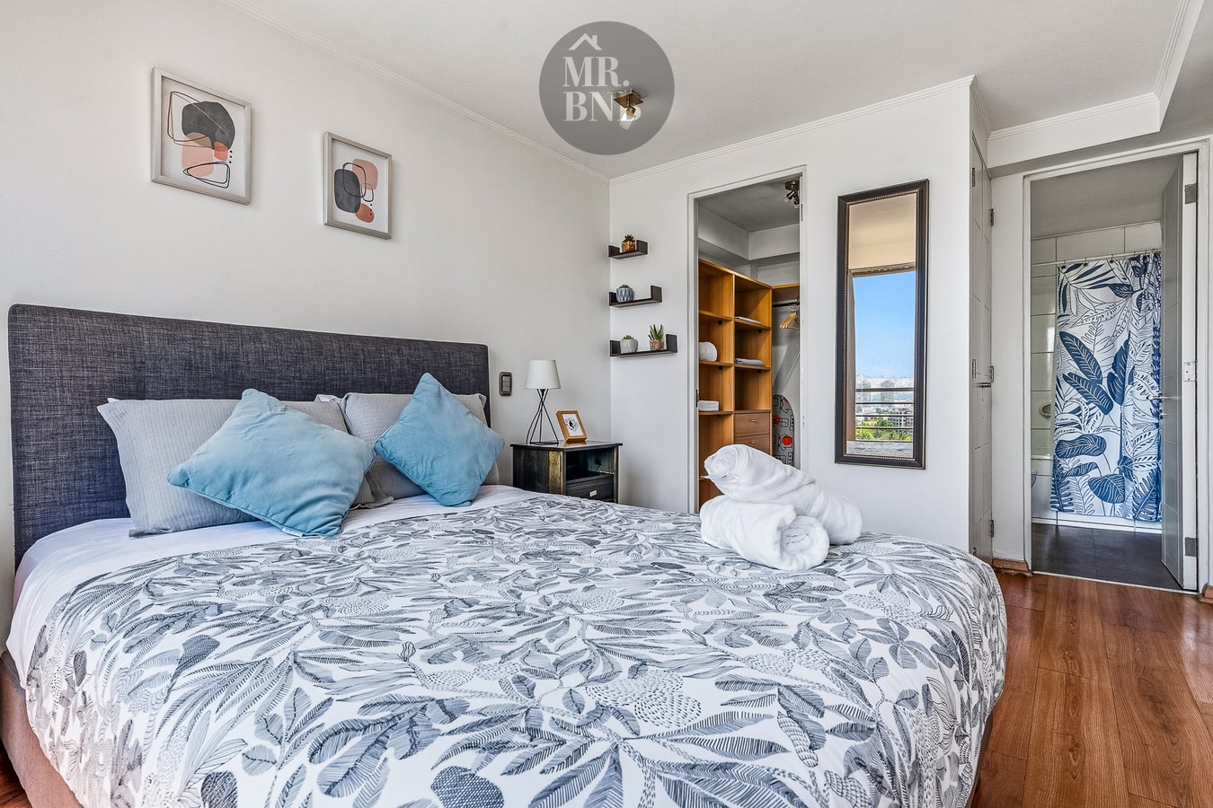 Dormitorio con cama, veladores con cojines y closet abierto con espejo.