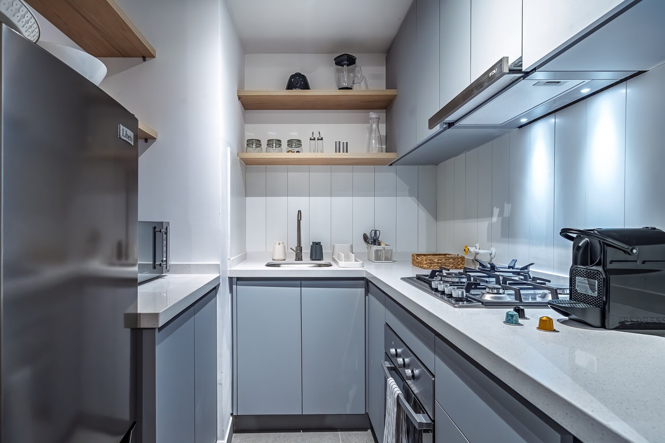 Cocina en L con muebles grises, cocina a gas y repisas de madera
