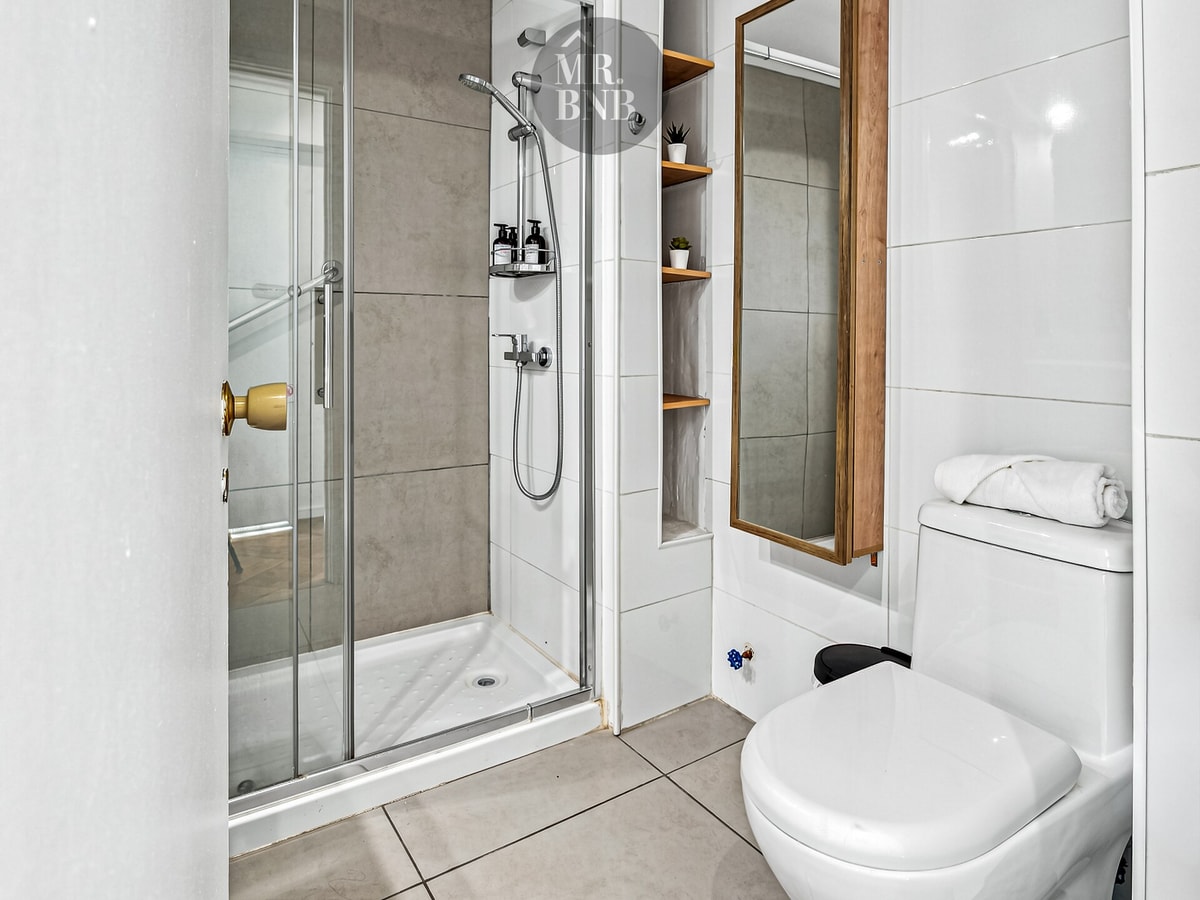 Baño con ducha de vidrio, inodoro, repisas y espejo