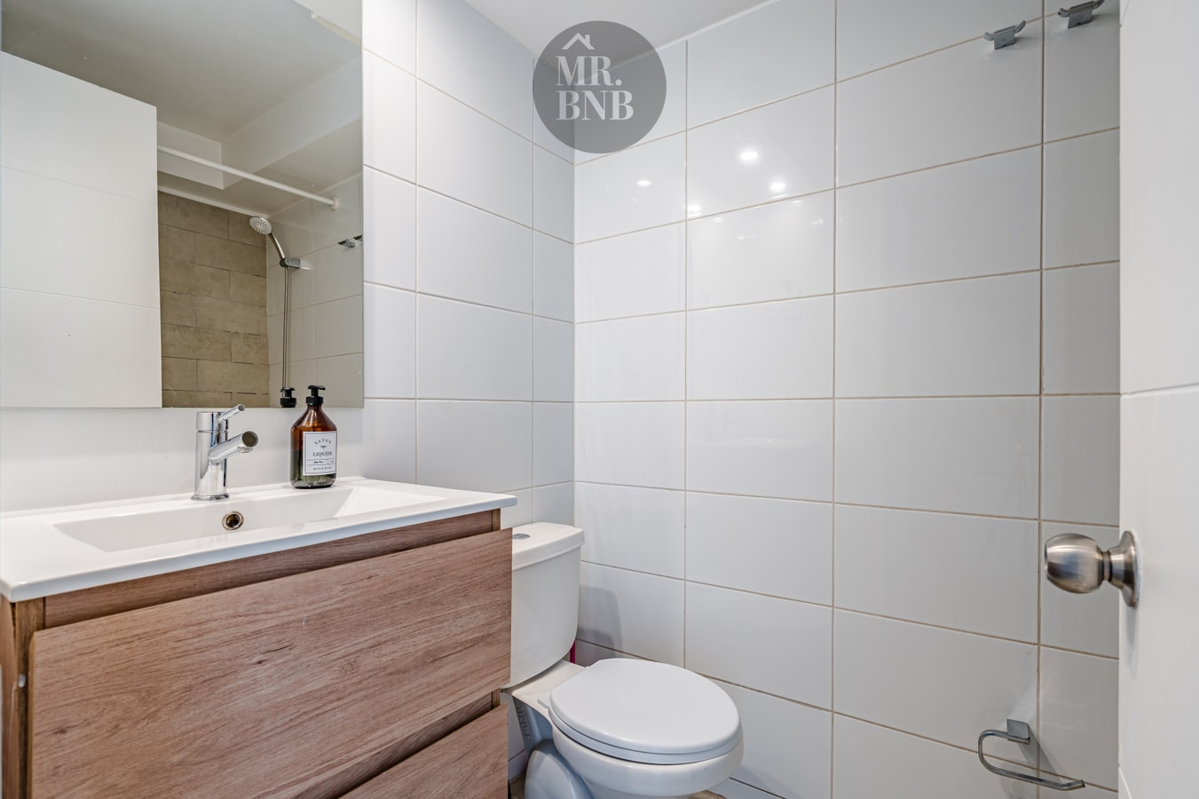Baño con lavamanos sobre mueble de madera, inodoro y ducha con puerta corrediza