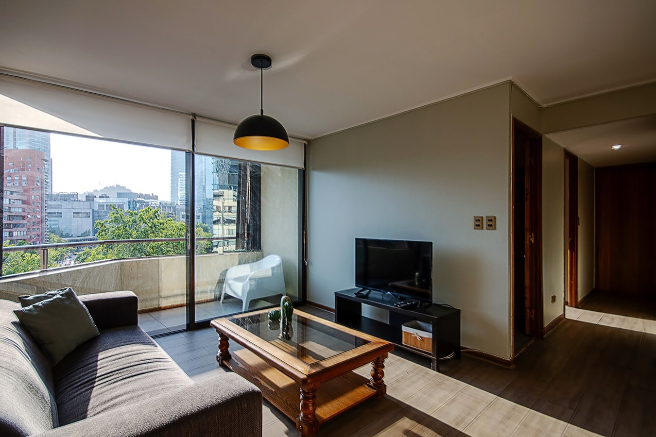 Living comedor con sofá, televisor y ventanal con vista a la ciudad.