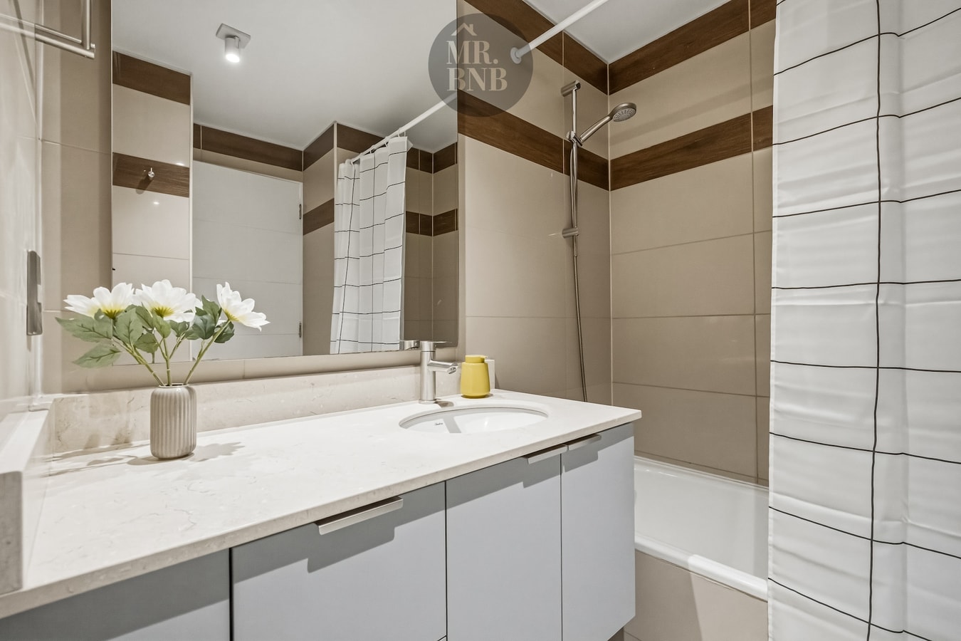 Baño con mueble vanitorio, espejo y flores sobre la encimera, cortina de tina al fondo