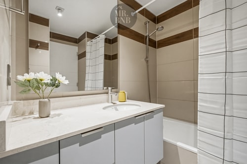 Baño con mueble vanitorio, espejo y flores sobre la encimera, cortina de tina al fondo
