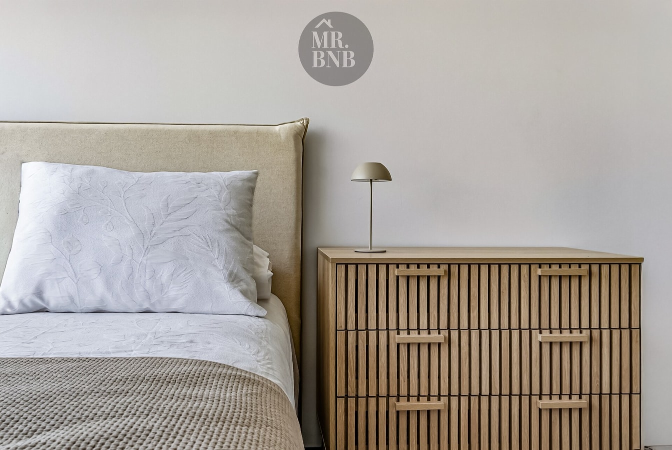 Dormitorio con cama, velador con lámpara y cómoda de madera