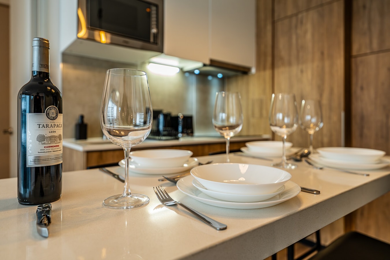 Mesón de cocina con servicio de bienvenida: vino, copas y vajilla dispuesta, campana extractora al fondo.