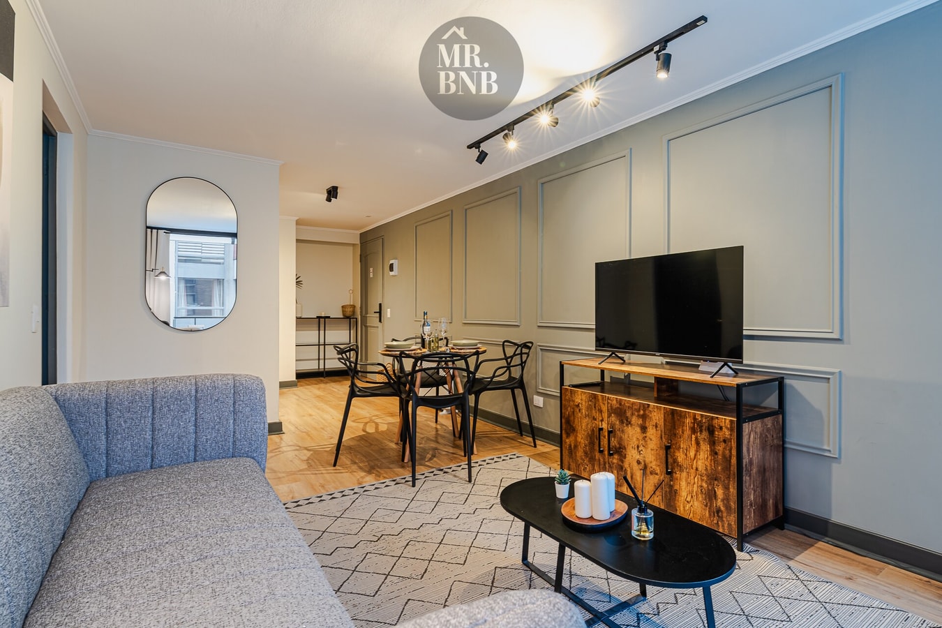 Living con sofá, TV, mueble bajo, mesa de centro, comedor al fondo y espejo redondo