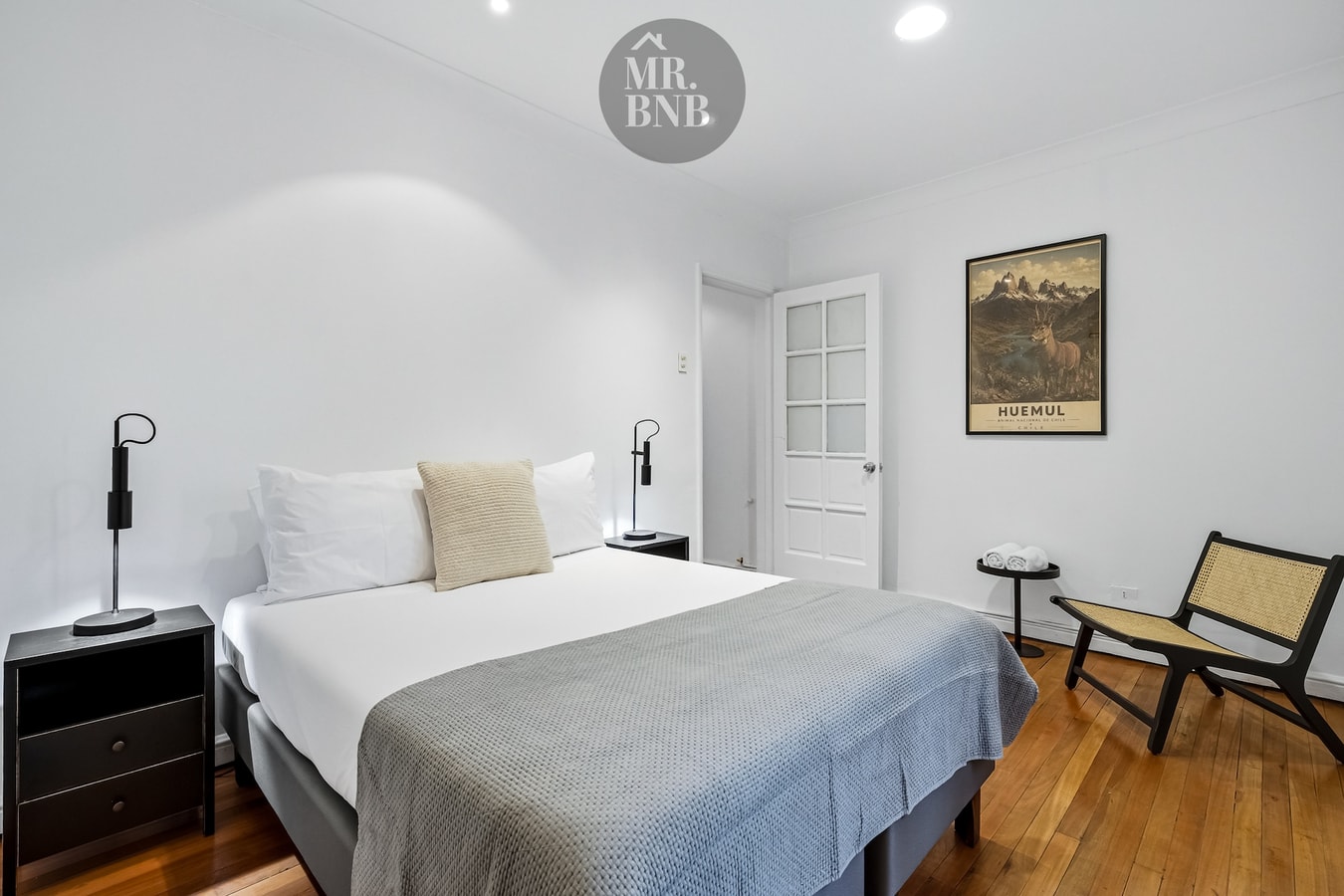 Dormitorio con cama de dos plazas, veladores a ambos lados y silla de madera.