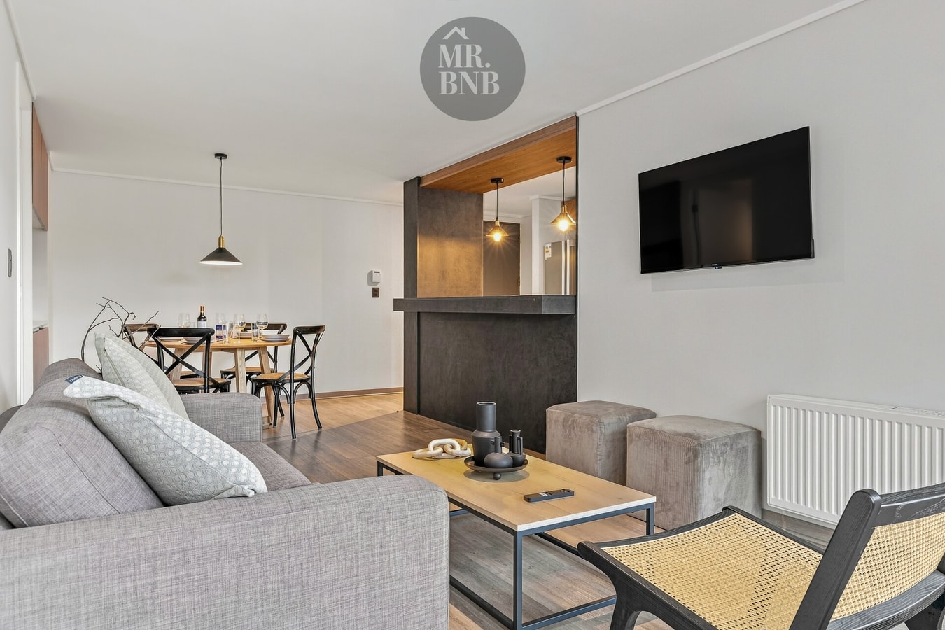 Living comedor con sofá, sillón de mimbre, mesa de centro y televisor en la pared