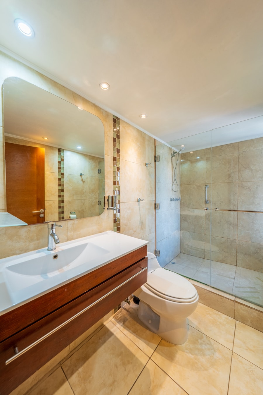 Baño con lavamanos, ducha con puerta esmerilada y piso de baldosas en tono café.