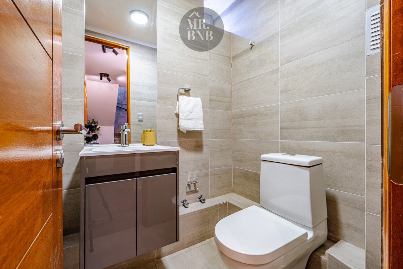 Baño con tina, azulejo color arena, inodoro y mueble vanitorio