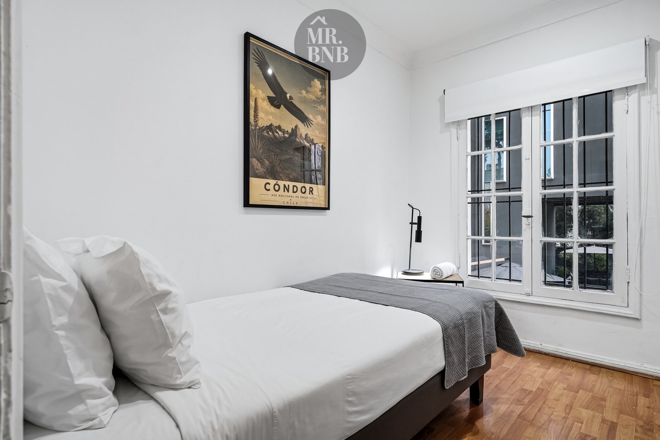 Dormitorio con cama de dos plazas, cuadro decorativo y ventana con rejas.