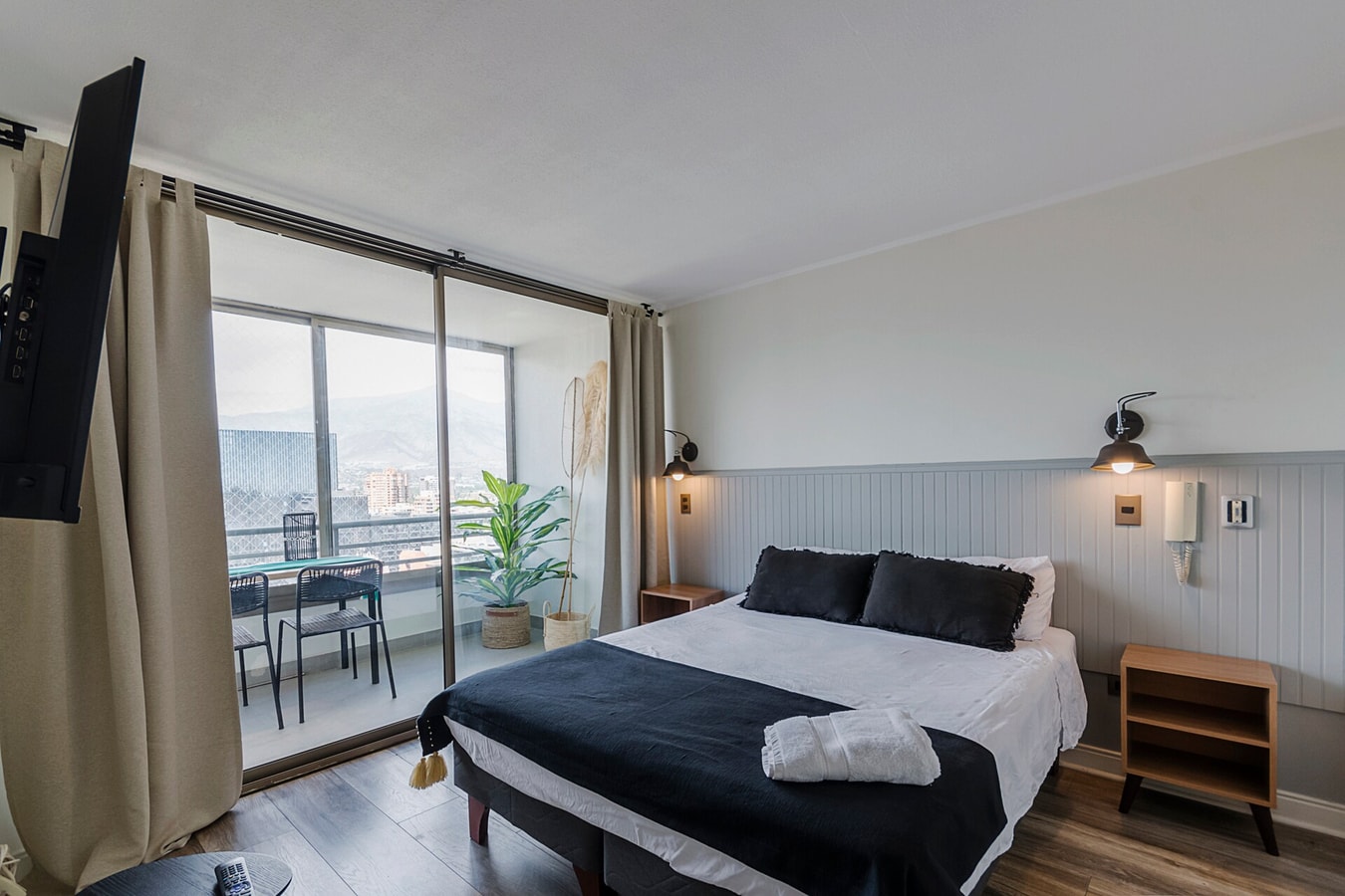 Dormitorio con cama, ventanal hacia terraza, cortina y TV