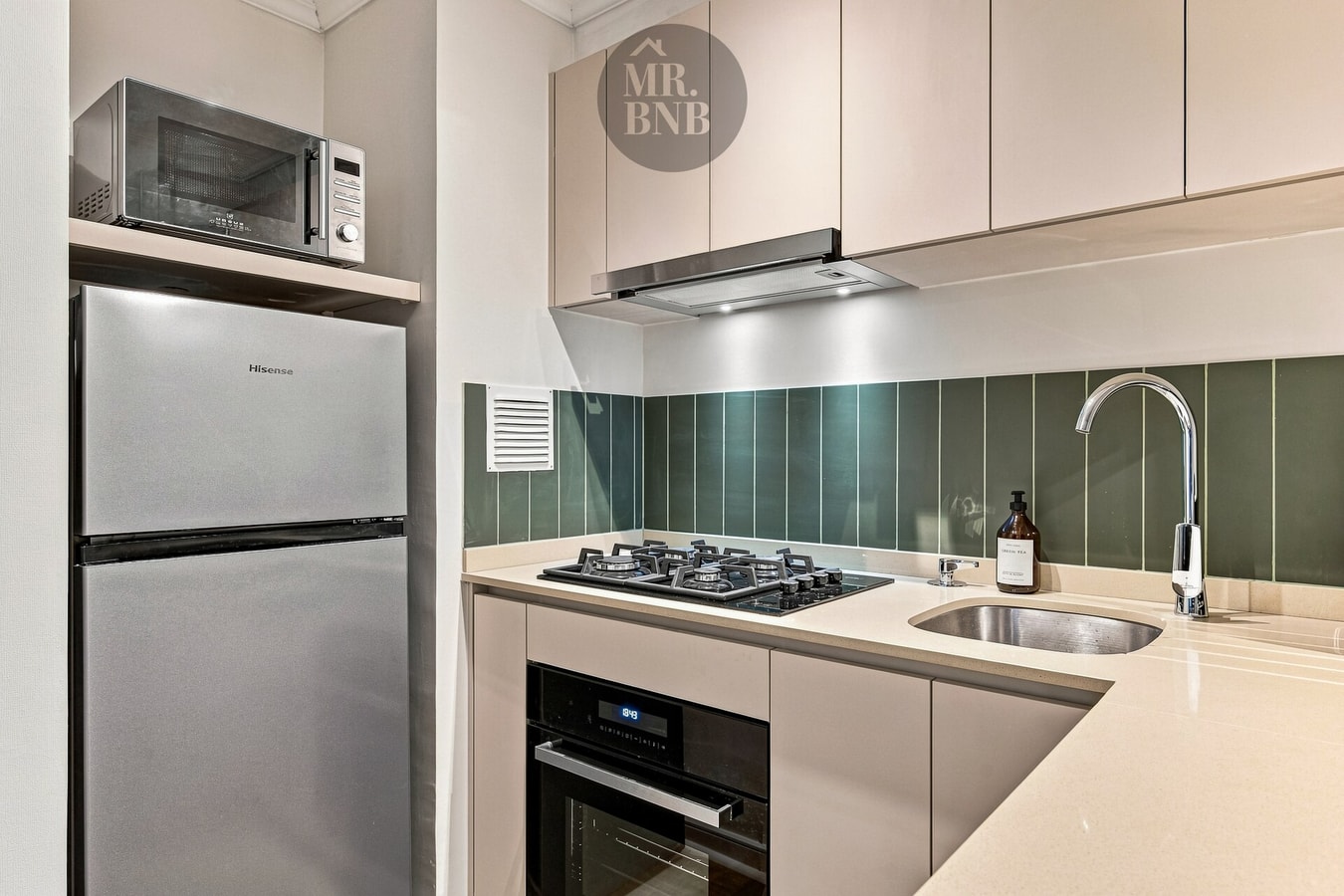 Detalle de cocina con microondas, campana, refrigerador, encimera a gas y lavaplatos