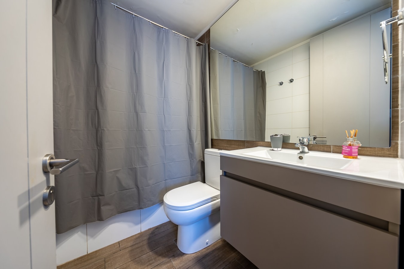 Baño con ducha con cortina, inodoro y lavamanos con mesón, iluminación cálida