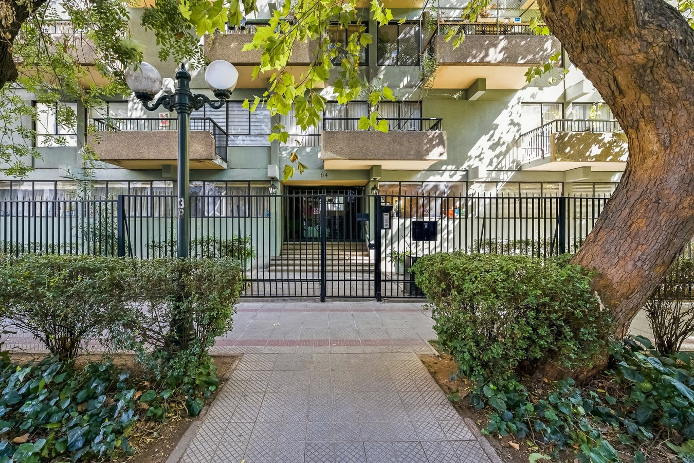 Fachada del edificio con jardín, reja de acceso y sendero