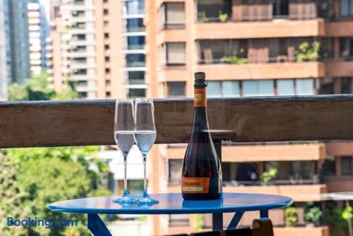 Terraza o balcón con mesa alta, copas y botella, con vista a edificios y vegetación