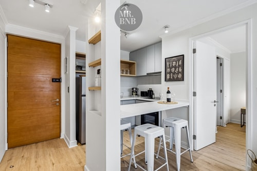 Hall de entrada con puerta de madera, columnas y vista hacia la cocina con banquetas