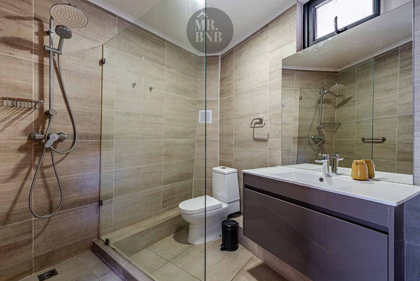 Baño con ducha de vidrio, inodoro y lavamanos con mueble oscuro