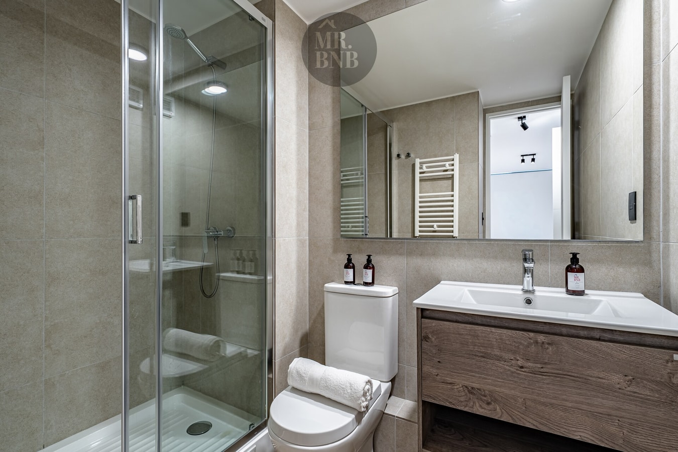 Segundo baño con ducha, vanitorio de madera y toallero calefactor.