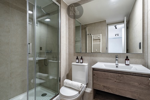 Segundo baño con ducha, vanitorio de madera y toallero calefactor.