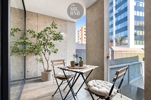 Terraza privada con mesa pequeña, sillas y planta, vista a edificios