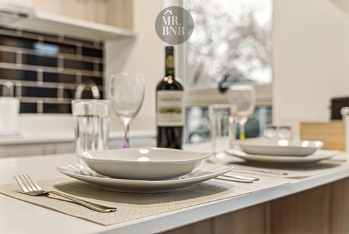 Detalle de mesa puesta sobre mesón de cocina, con copas, platos y una botella de vino
