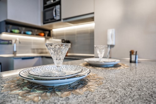 Detalle de mesa puesta sobre el mesón de la cocina, con vajilla, copas y plato decorativo bajo luz cálida