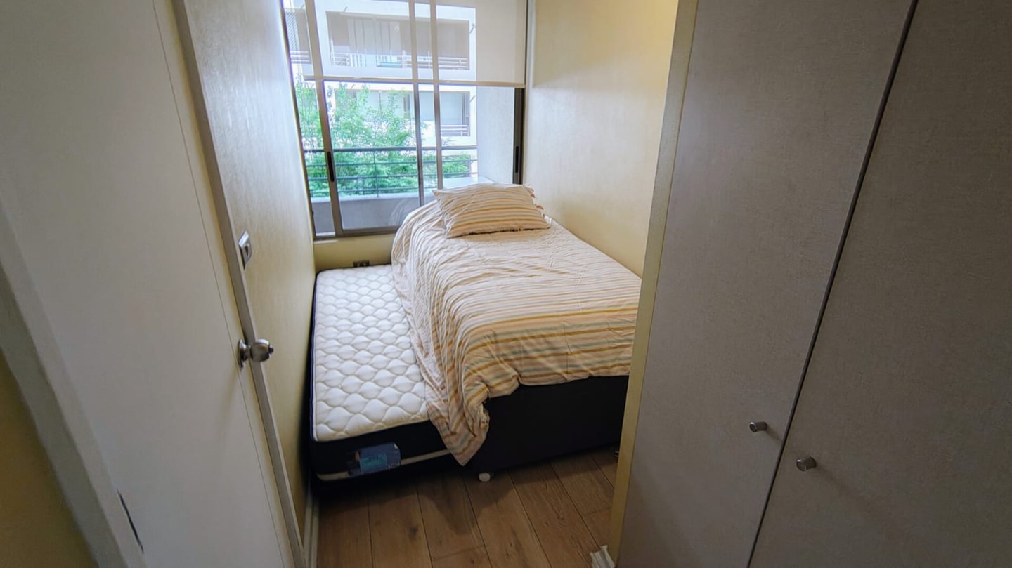 Dormitorio angosto con cama de una plaza, ventana con vista a los árboles y clósets empotrados a ambos lados