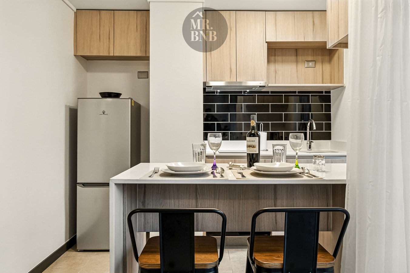 Cocina con mesón blanco, banquetas negras y mesa puesta con vajilla y copas de vino