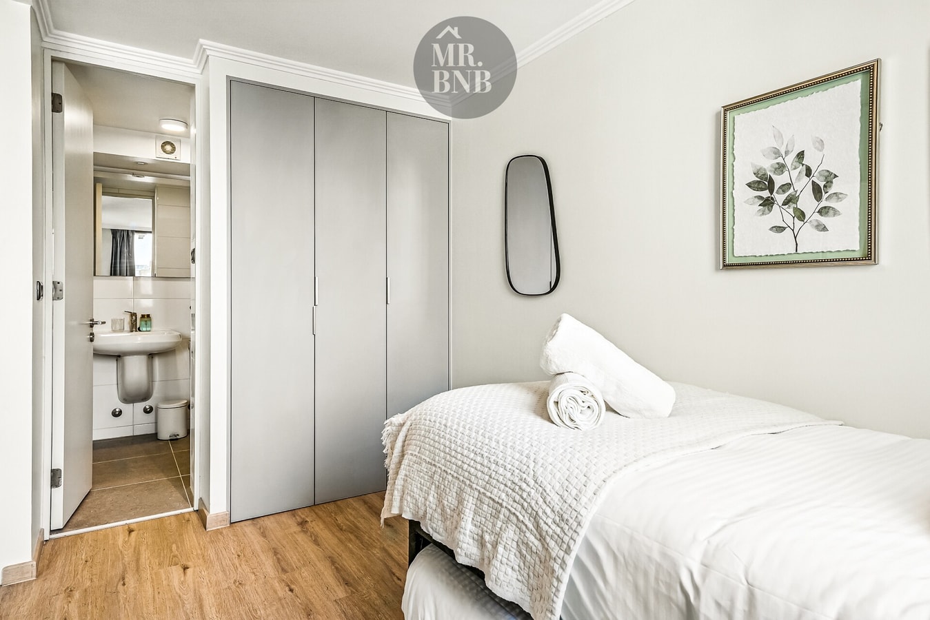 Dormitorio con cama, closet abierto, espejo y puerta hacia el baño.