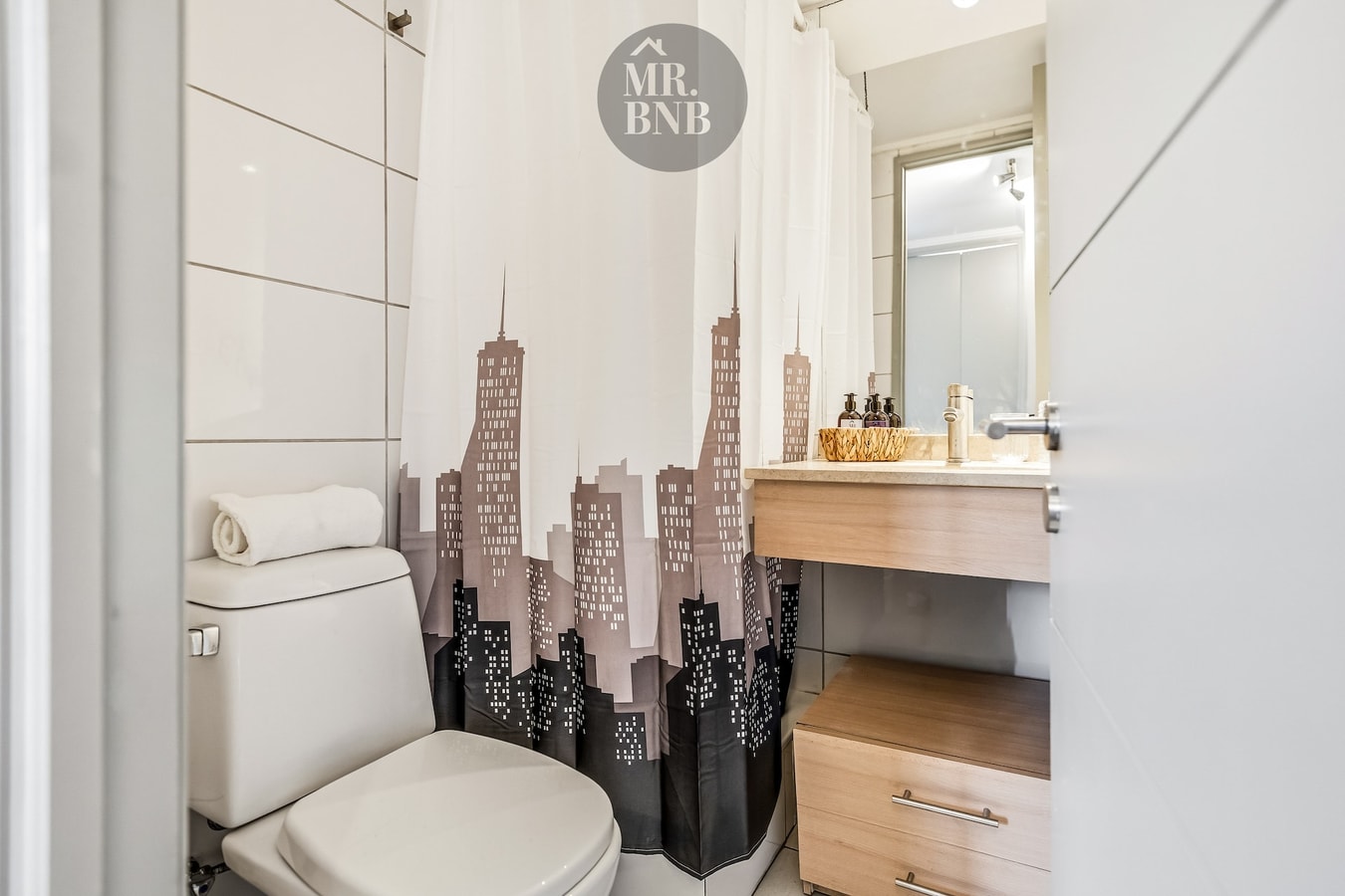 Baño con cortina de ducha con estampado urbano, inodoro y mueble de vanitorio.
