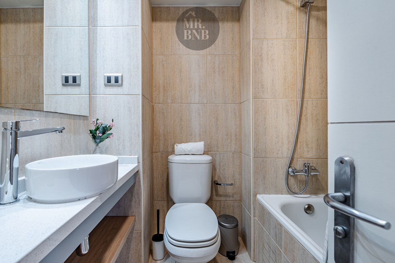 Baño con lavamanos sobre mueble de madera, inodoro y tina con ducha telefónica