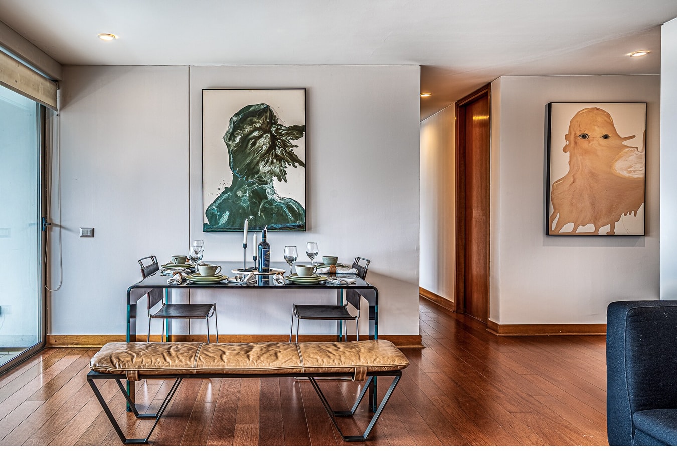 Comedor con mesa puesta y living al fondo, obras de arte en las paredes.