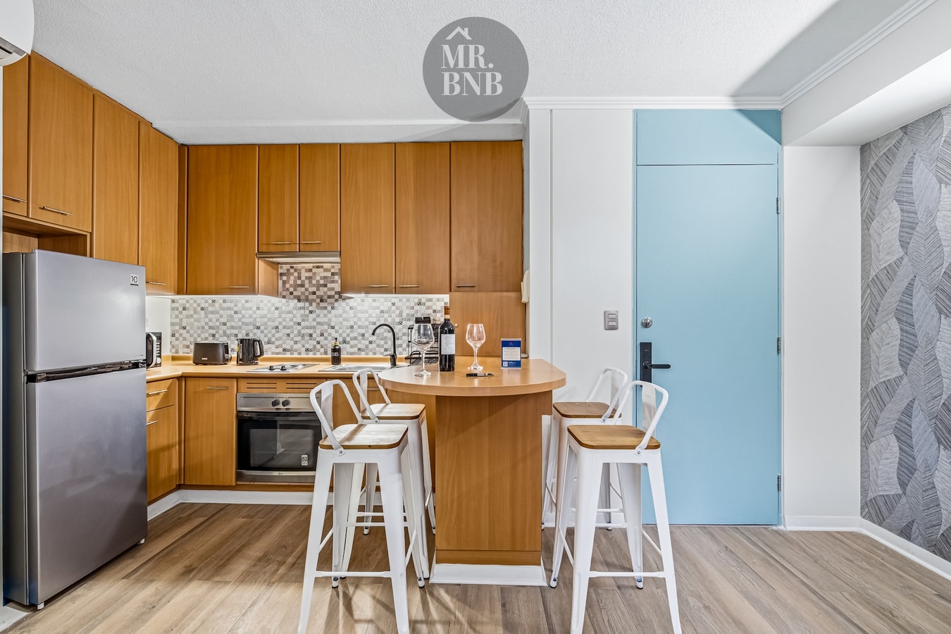 Cocina con isla, taburetes blancos, refrigerador y puerta celeste