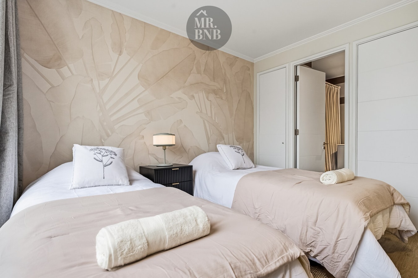 Dormitorio con dos camas individuales, velador y ventanal con vista a la ciudad