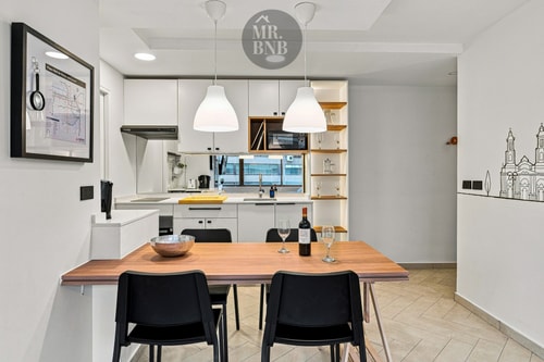 Comedor con mesa de madera, sillas negras y cocina integrada con ilustración en la pared.