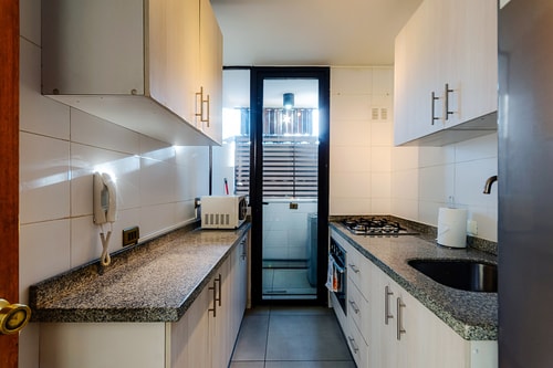 Cocina en L con encimera de granito, cocina a gas y ventana hacia el pasillo.