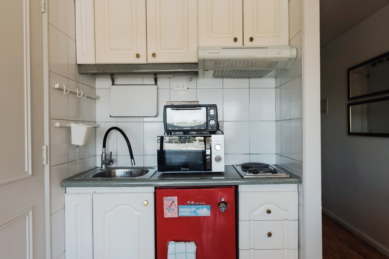 Kitchenette blanca con microondas, cocinilla y refrigerador rojo bajo mesón