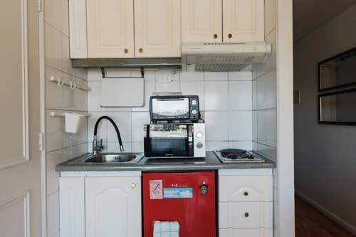 Kitchenette blanca con microondas, cocinilla y refrigerador rojo bajo mesón