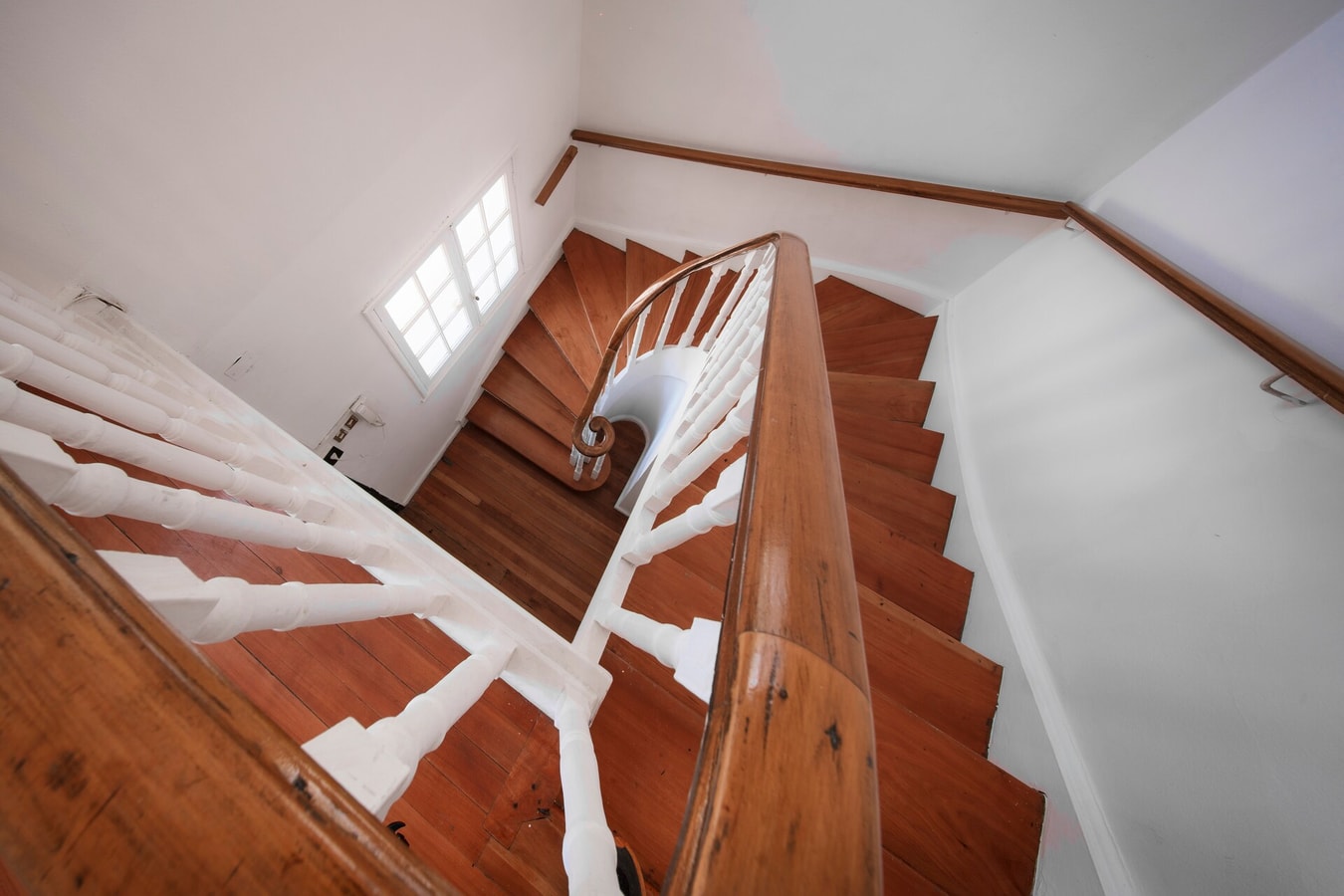 Escalera de madera con pasamanos curvo y balaustres blancos, vista desde el descanso superior