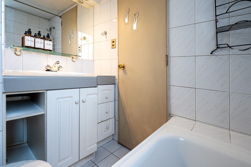 Baño con lavamanos, mueble bajo con cajones y bañera de tina revestida en cerámica clara.