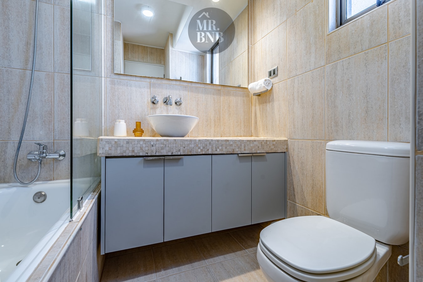 Baño con lavamanos, espejo, mueble gris, inodoro y tina