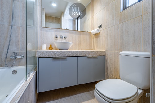 Baño con lavamanos, espejo, mueble gris, inodoro y tina