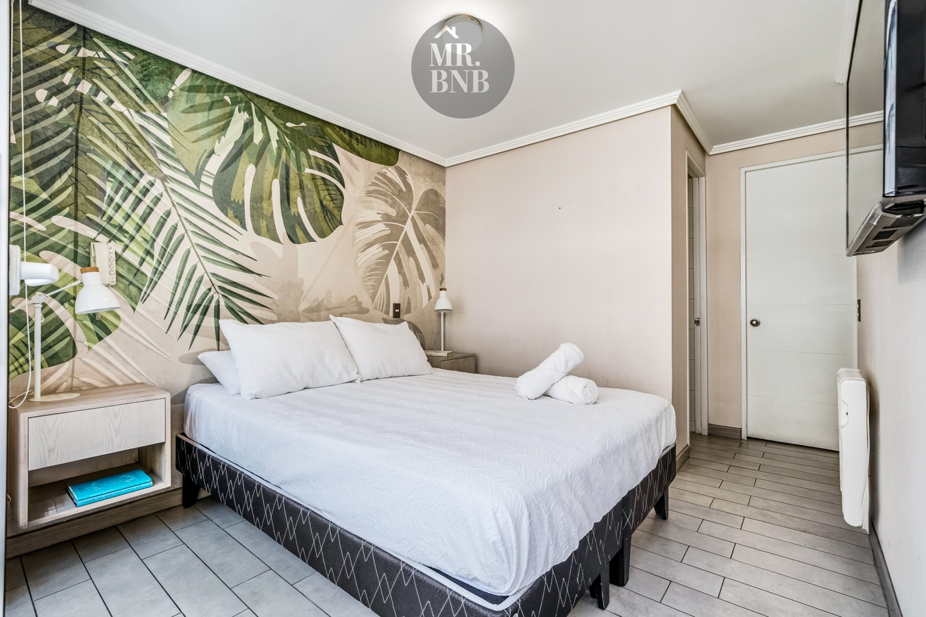 Dormitorio con cama, velador y papel mural con estampado tropical.