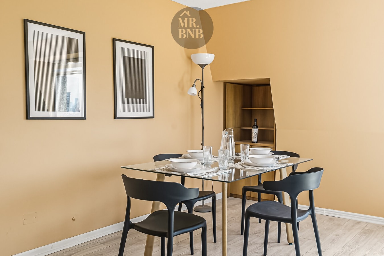 Comedor con mesa de vidrio, sillas negras y cuadros en la pared