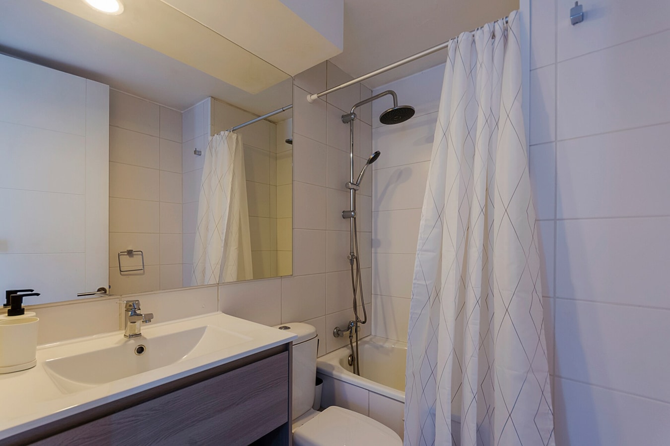 Baño con tina, cortina, lavamanos y espejo grande