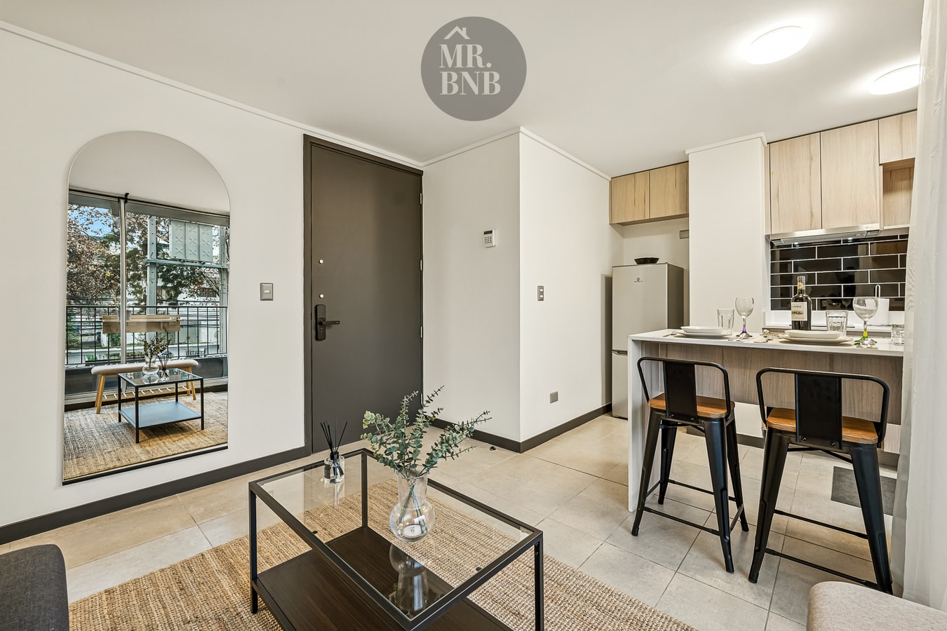 Living con arco decorativo, espejo, mesa de centro de vidrio y cocina con banquetas al fondo